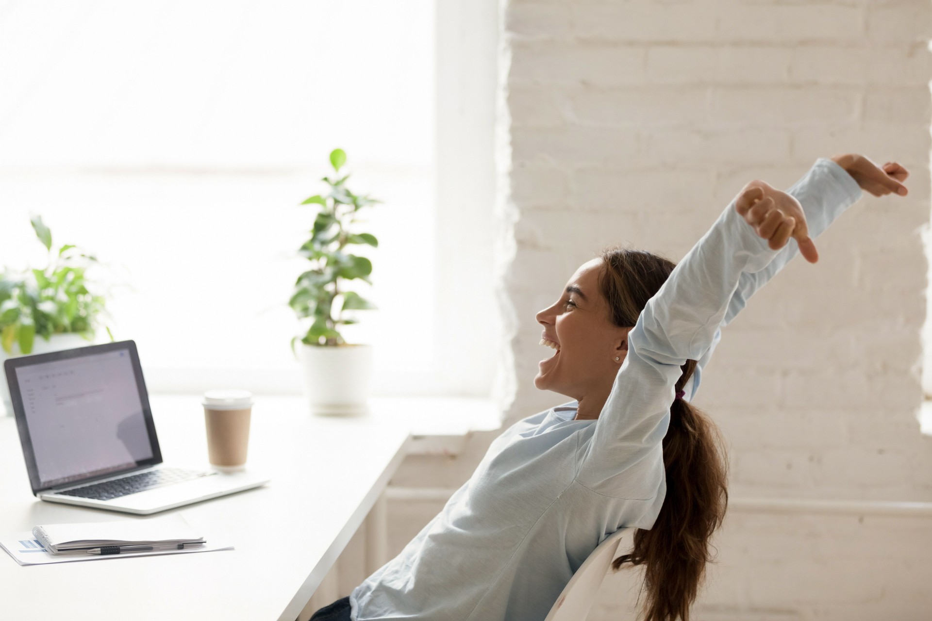 Cheerful woman stretching raising hands up sitting at workplace