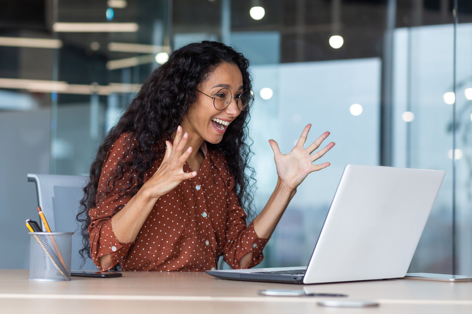 Young hispanic business woman got good work result, business woman is happy and celebrating victory holding hands up looking and reading from laptop screen